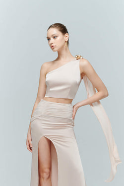 Woman modeling the Seraphine asymmetrical top, showcasing the sculptural lines and ethereal flowing silk ribbon draping over the arm.