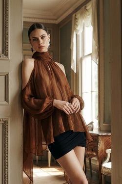 Woman in aurorette brown sheer mesh top and black skirt standing in a sunlit room.
