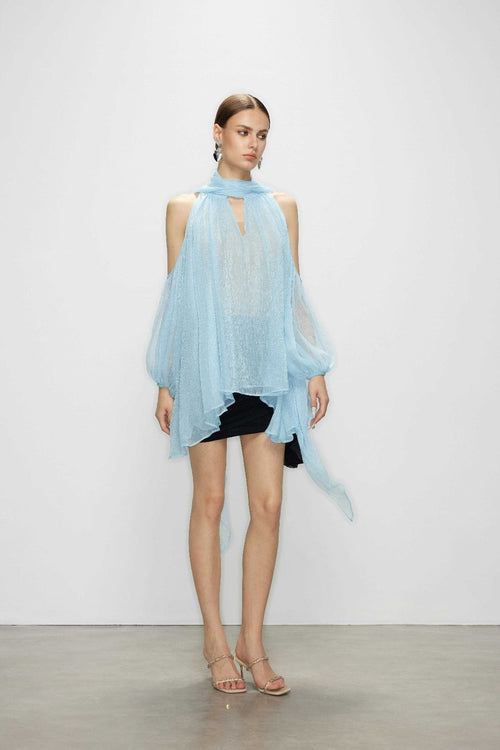 Model wearing the Aurorette light blue tulle cold shoulder blouse featuring a high neck tie and sheer airy drape