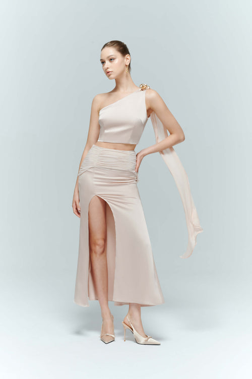 A model walking to showcase an elegance skirt made of light pink satin, highlighting the flowy drape of the slit skirt