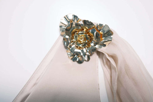 Close-up macro detail of the solid gold-toned metal floral embellishment on the Seraphine pink asymmetrical top.