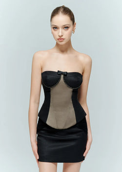 Model facing forward wearing the Marcelline strapless black corset top, featuring a contrast front panel and delicate beaded bow detail, styled with a black mini skirt.