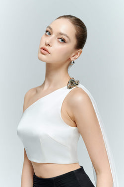 Close-up of the Seraphine sleeveless crop top in white, showcasing the flattering asymmetrical neckline and solid silver-toned metal floral embellishment.